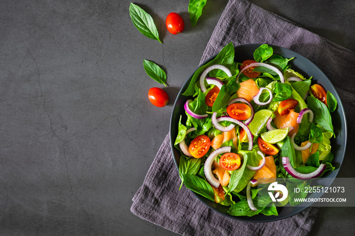 Salmon salad, view from above fresh tomato, onion, spinach, lettuce , basil in black bowl on napkin with dark backgrond. Healthy food, home made concept. Tasty and meal. Top view, copy space.