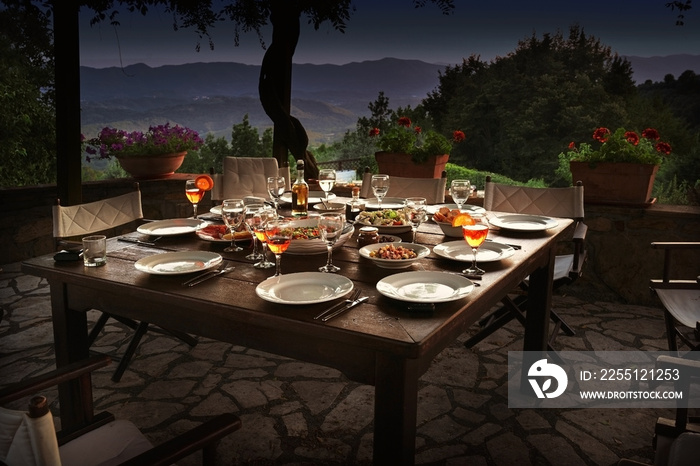 large rustic table on a garden terrace prepared for a dinner party at night