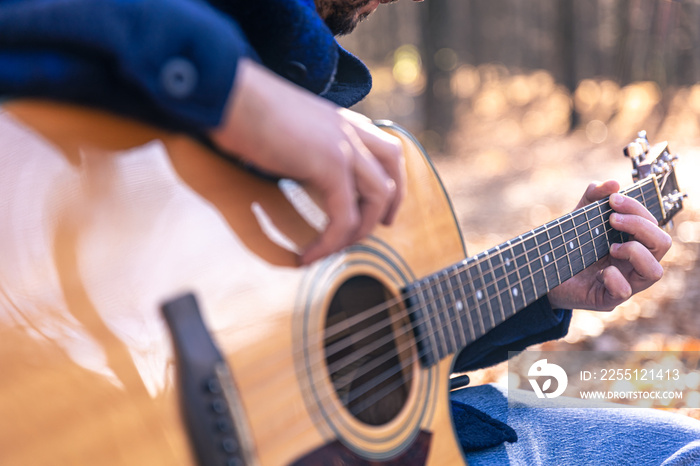 Close-up, a man plays an acoustic guitar in the autumn forest.