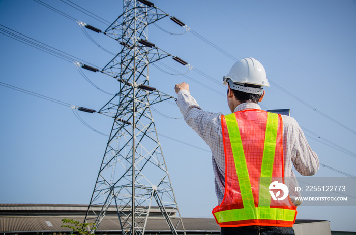 Electrical engineer holding and using a digital tablet, Engineer pointing at high voltage power pylon against sunset background