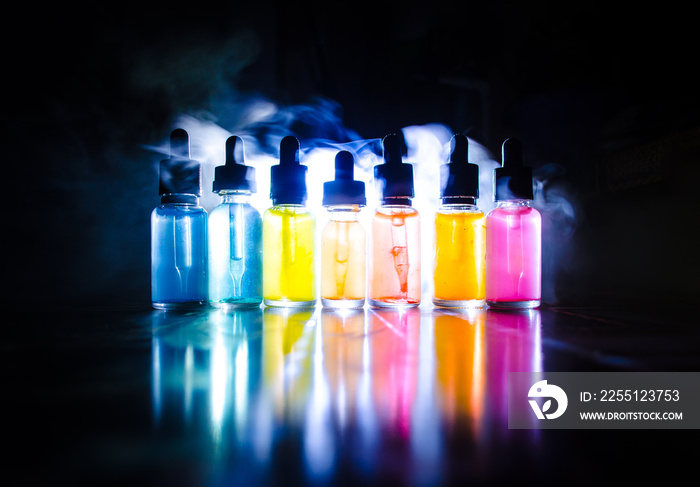 Vape concept. Smoke clouds and vape liquid bottles on dark background. Light effects. Useful as background or vape advertisement or vape background. Selective focus