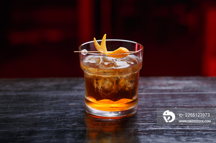 Closeup of a God father cocktail in short glass, gin, standing on the bar counter, isolated on a red light background. Horizontal view.