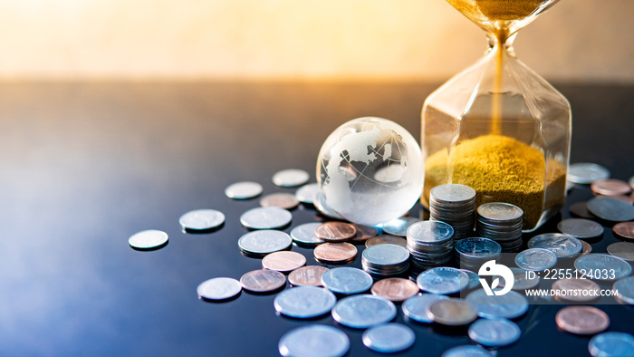 Global business investment growth. Wealth concept. Gold sand running through the shape of modern hourglass with world globe crystal glass and US dollar coins on blue reflective table.