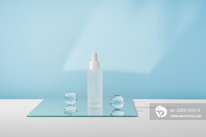 Serum cosmetic bottle with peptides and retinol on mirror with glass balls on blue background. Hyaluronic acid cosmetics product mock up packaging with stylish props. Serum beauty dropper mockup