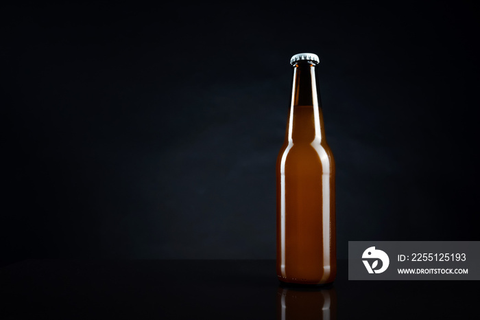 Cold unopened bottle of beer with cap on black background. Glass of refrigerated wheat or lager beer on dark background