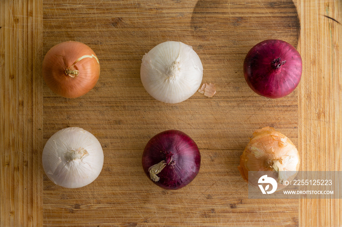 Six red, brown and white onions on a bamboo board