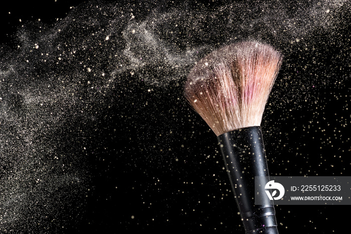 cosmetic brush and sprayed cloud of cosmetics on a black background