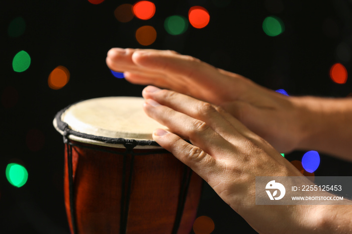 Hands of man playing African drum against defocused lights, close up