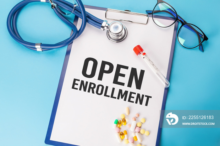 OPEN ENROLLMENT. Stethoscope and paper plate with a sheet of white paper with text OPEN ENROLLMENT blue backround. Medical concept