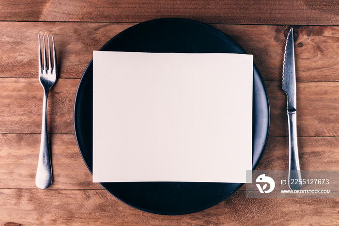 Lunch invitation, consisting of a black plate and cutlery on a wooden table.