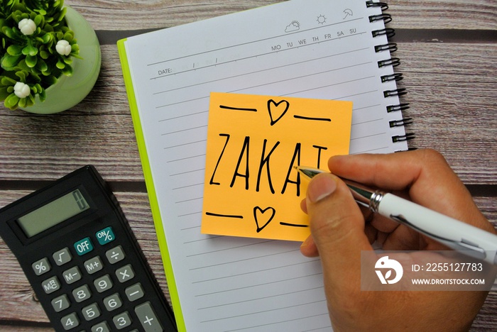 Calculator, flower, sticky note and hand write word ZAKAT. Zakat is muslim tax to help each other.