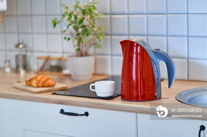 Modern red electric kettle with a с white cup on the table in the kitchen at home