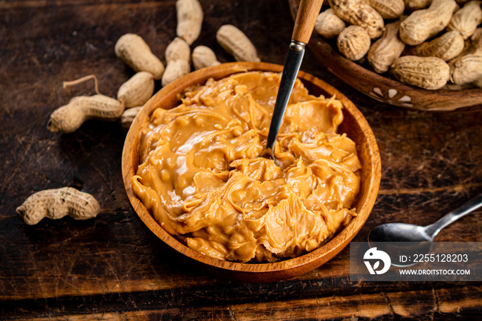 Peanut butter and inshell peanuts on a cutting board.