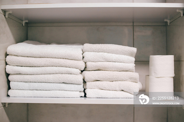 Clean towels on shelf in bathroom. White towels on the shelf. Toilet paper rolls in the closet.