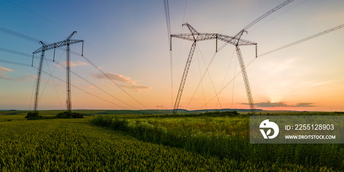 Dark silhouette of high voltage towers with electric power lines at sunrise