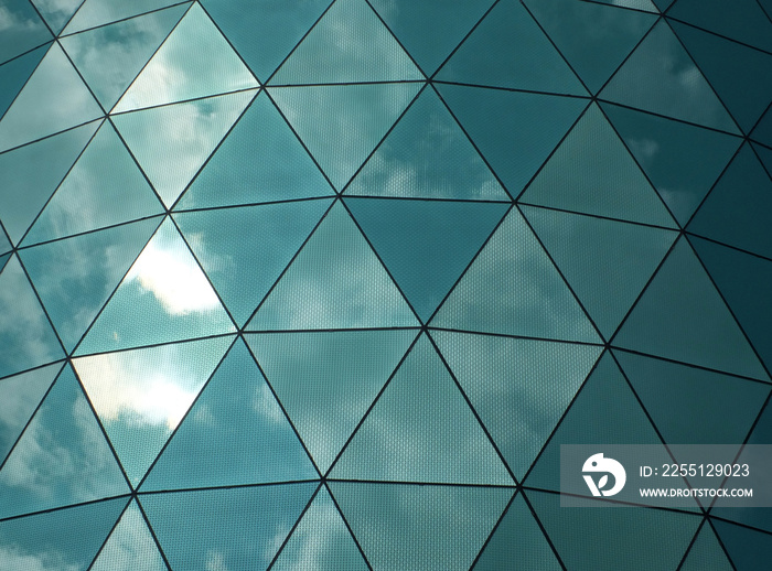 angular mirror cladding on a modern structure with reflected sky and clouds