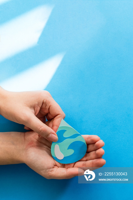 Woman hand holding paper cut water drop on blue background. Clean water and sanitation, saving water. World Water Day. Ecology concept.
