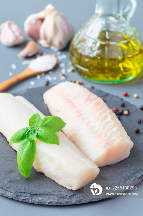 Fresh raw cod fillet with spices, pepper, salt, basil on stone plate, vertical