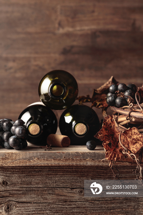 Bottles of red wine with grapes and dried vine on an old wooden table.