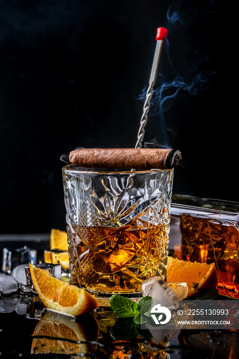 Glass of whiskey with smoking cigar and ice cubes on a black background. concept luxury drink cocktail