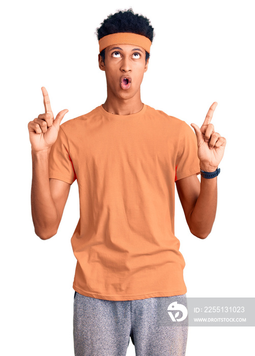 Young african american man wearing sportswear amazed and surprised looking up and pointing with fingers and raised arms.