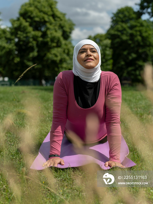 UK,Sutton,Woman in headscarf practicing yoga in grassy field