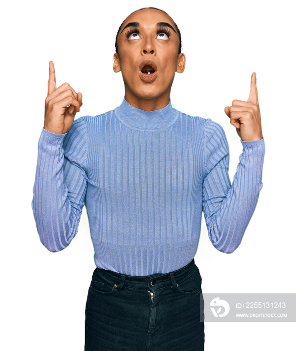 Hispanic transgender man wearing make up and long hair wearing casual clothes amazed and surprised looking up and pointing with fingers and raised arms.