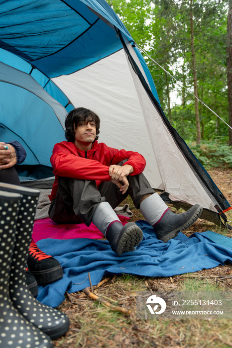 Young man sitting in tent and putting on rain boots