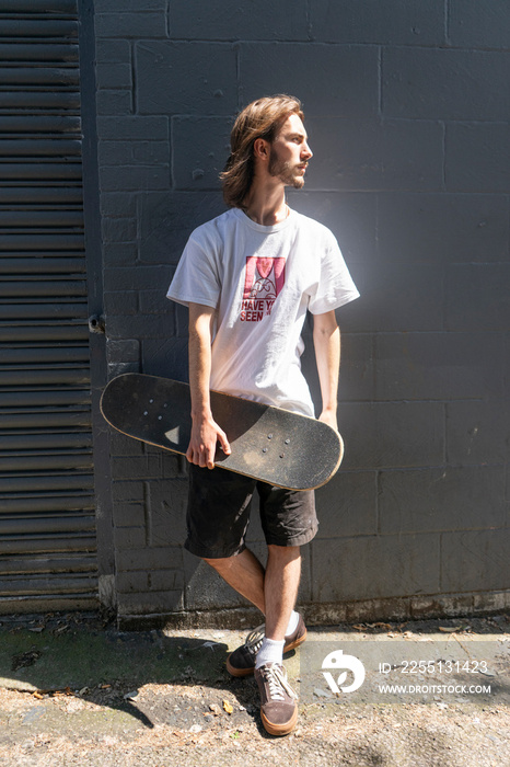 Young man standing outdoors holding skateboard