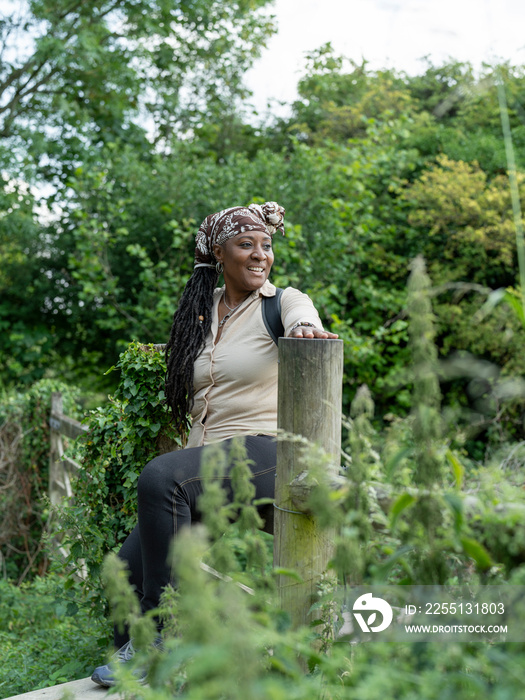 Smiling mature woman sitting on fence on hike