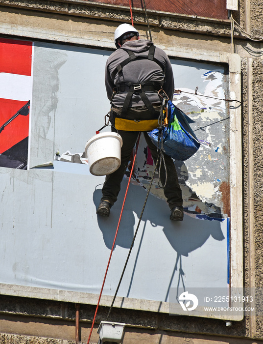 Worker puts a new poster on the wall hanging in high