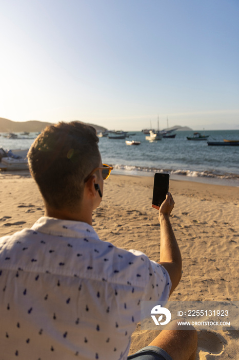 Man wearing earbuds using smart phone at beach