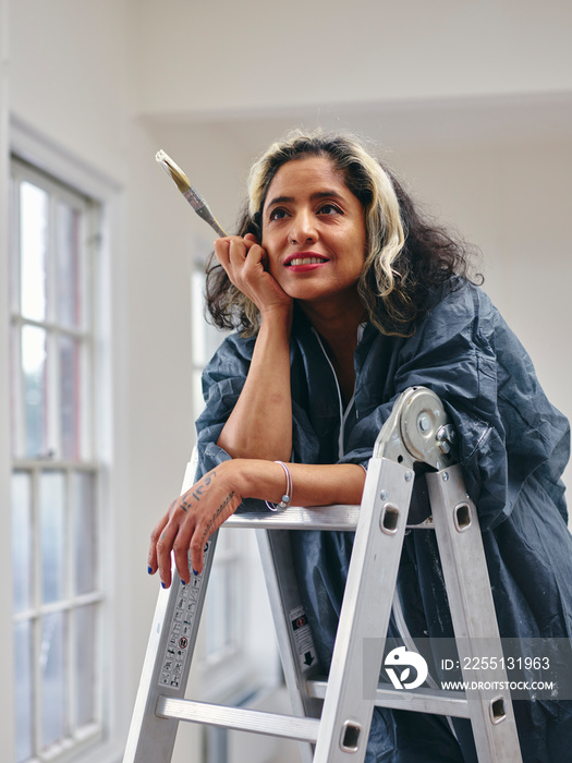 Smiling woman standing on ladder with paintbrush