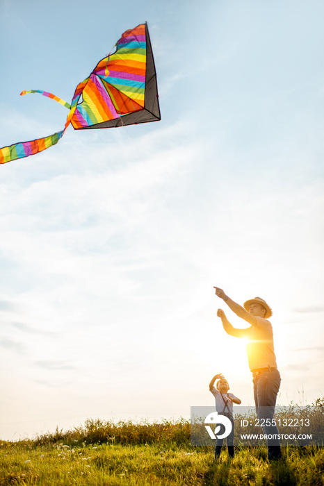 Father with son launching colorful air kite on the field during the sunset. Concept of a happy family having fun during the summer activity