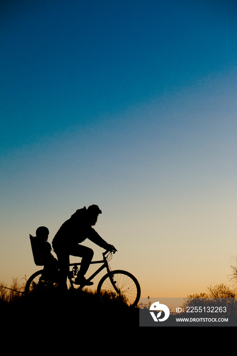 A silhouette of a father and his child ona bicycle during the sunset.