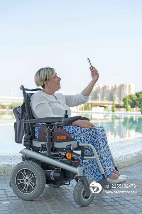 vertical portrait of a smiling disabled woman in a wheelchair taking a selfie photo in the city