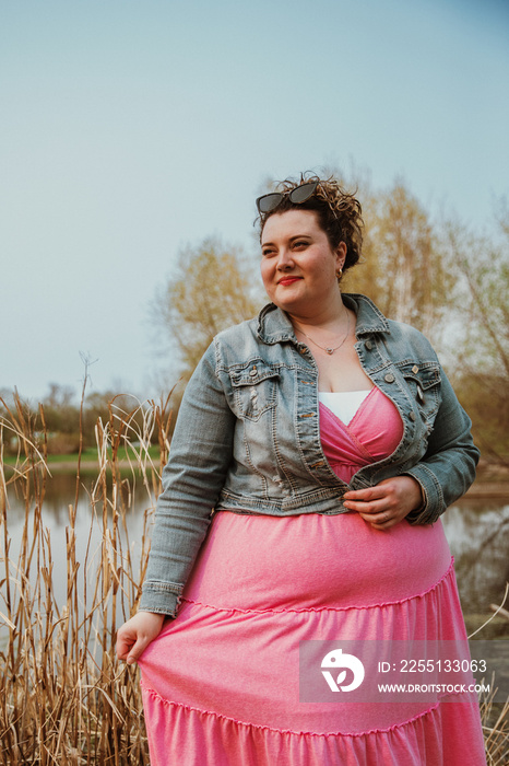 plus size woman stands in park with pink dress