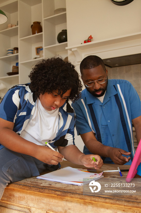 Plus sized child doing homework with his dad in the kiitchen