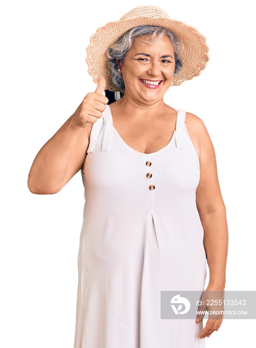 Senior woman with gray hair wearing summer hat and summer clothes smiling happy and positive, thumb up doing excellent and approval sign