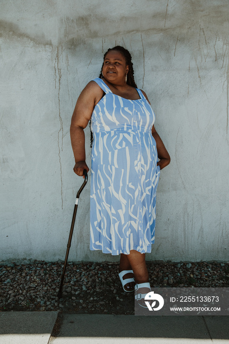 full body afro latinx haitian american woman stands against wall holding black cane