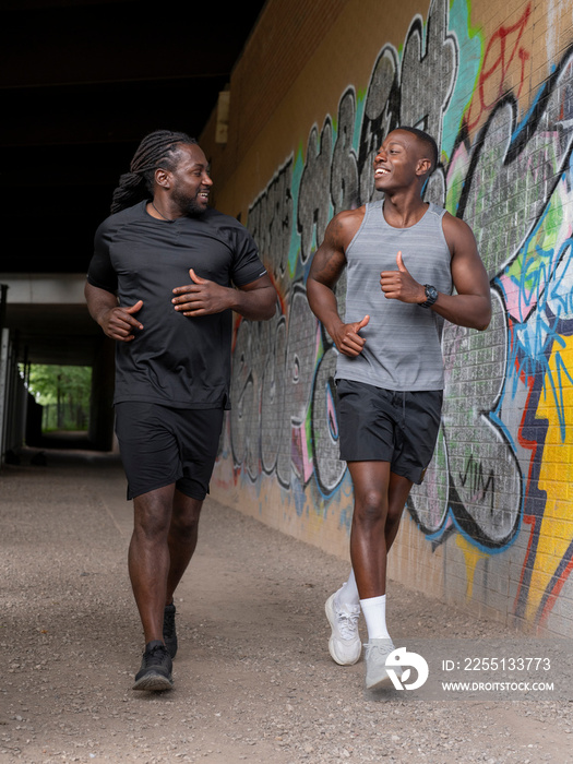 Two men jogging under bridge