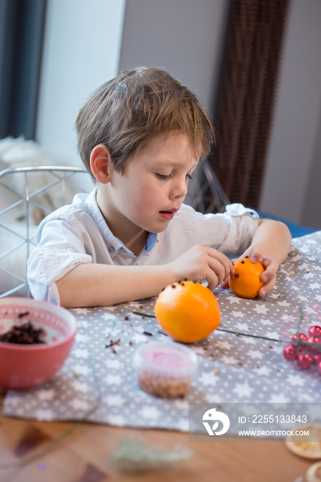 Little boy making orange pomander for Christmas season.  Simple idea for kid friendly festive crafts.