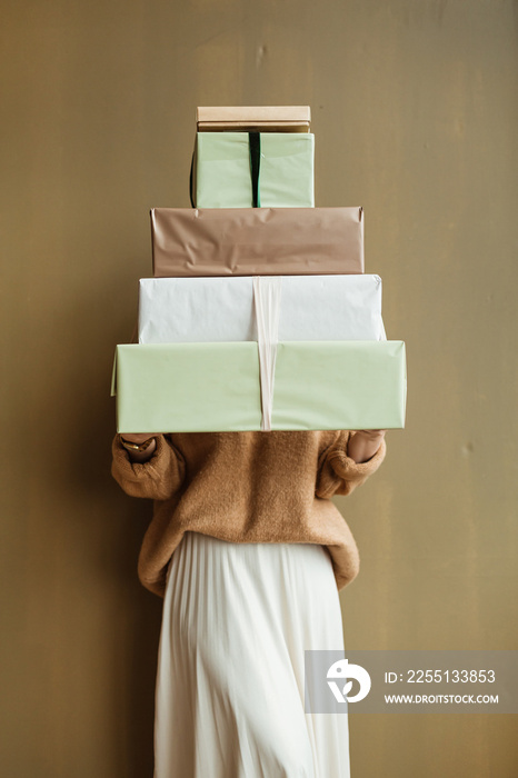 Young beautiful woman holding handmade paper gift boxes stack against olive wall. Minimal fashion festive Christmas / New Year celebration concept.