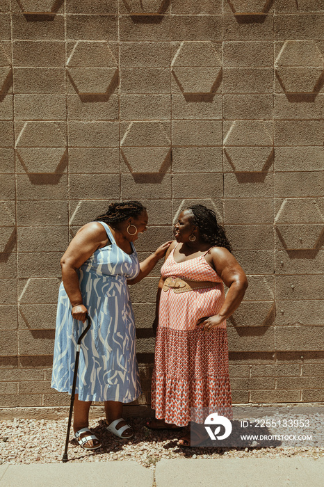 2 plus size African American women talk and laugh standing against a wall