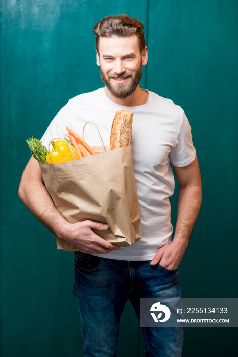 Handsome man holding a paper bag full of healthy food on the green background