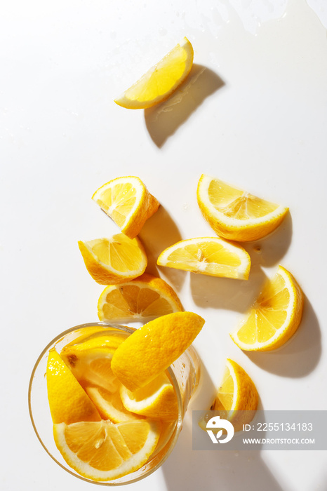 Lemons cut into pieces and a glass with natural lemonade on a white background. Top view.