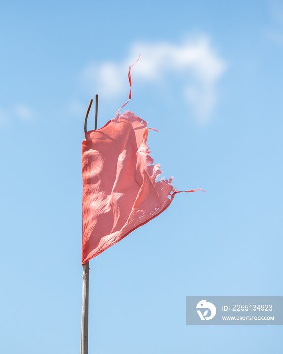 Red torn old flag on the sea against the blue sky.