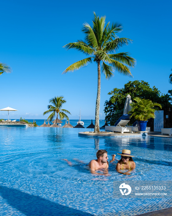 Beautiful tropical beachfront hotel resort with a swimming pool, sun-loungers, and palm trees , a paradise destination for vacations. couple men and woman mid age on a luxury vacation