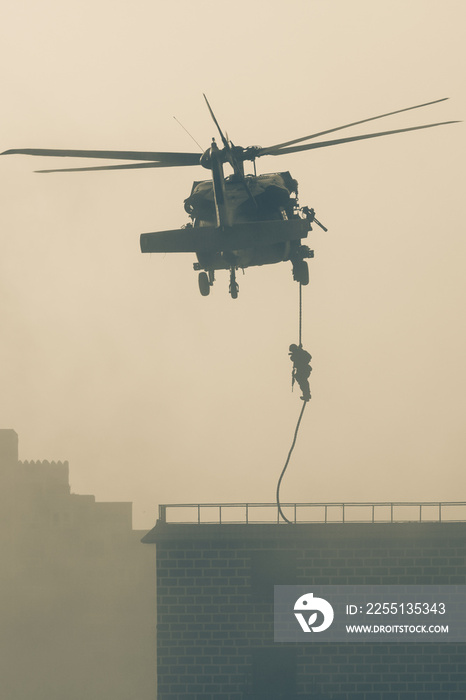 Military combat and war with helicopter flying into the chaos and destruction. Soliders suspend from rope to the ground from chopper. Military concept of power, force, strength, air raid.
