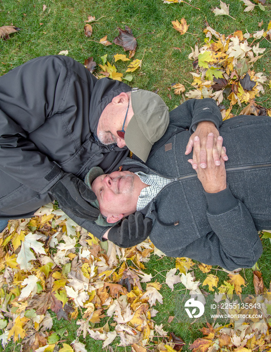 Gay senior married couple laying on the grass in an intimate moment taking a break from their back yard cleanup.